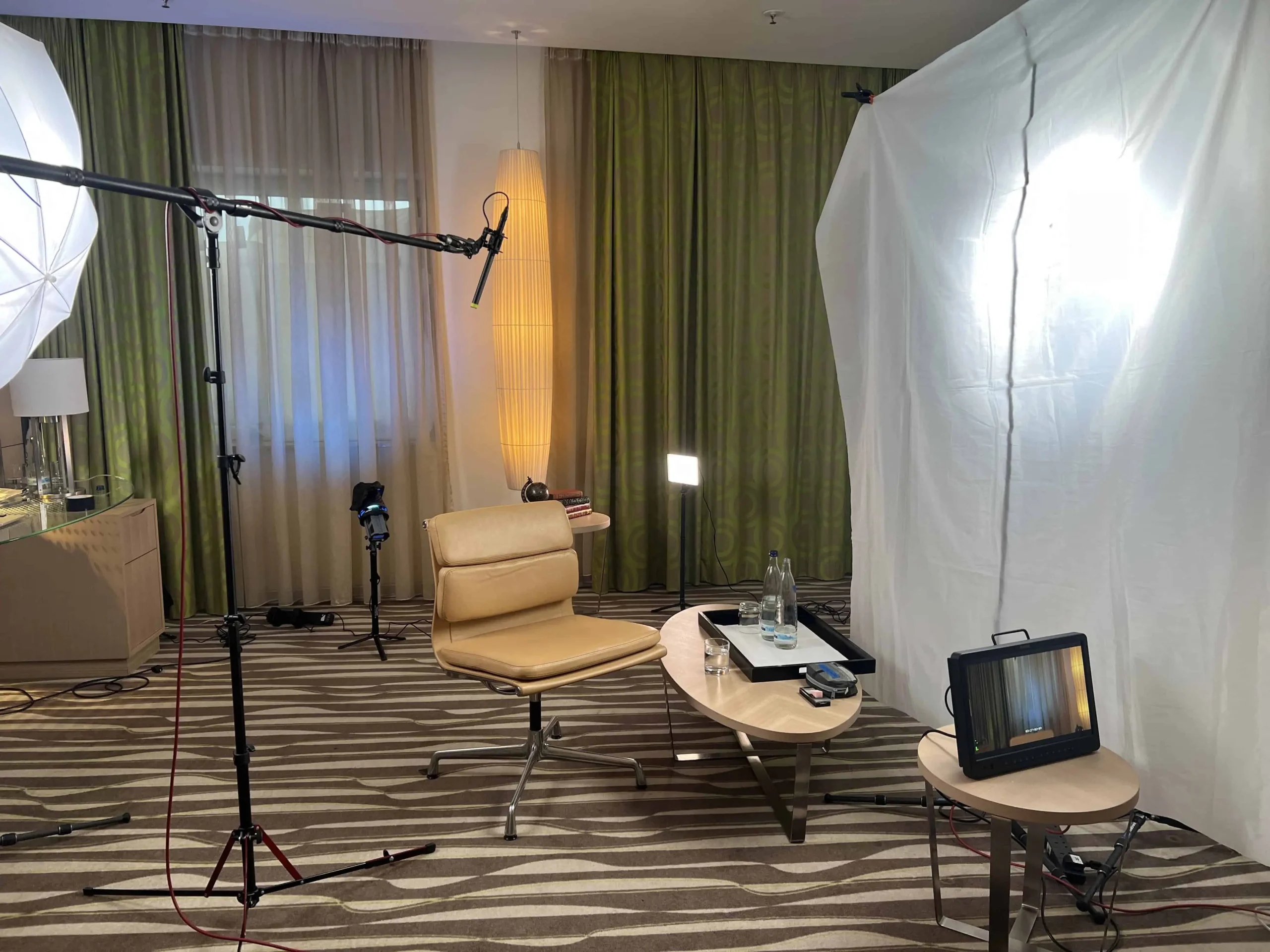 Interview setup with lighting rigs, chair, and monitor arranged in hotel room studio