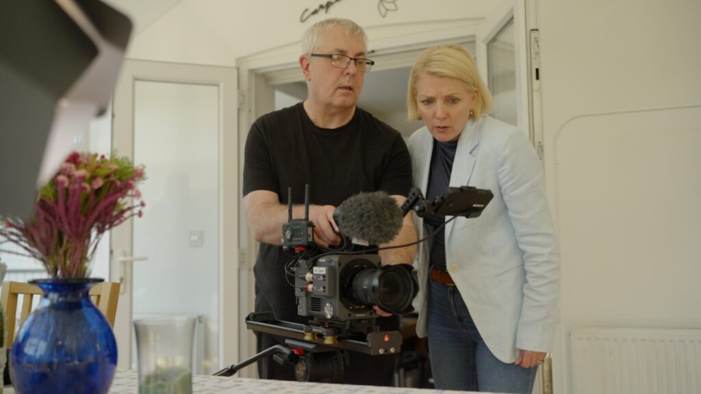 Documentary crew reviewing footage on camera monitor with presenter beside kitchen table