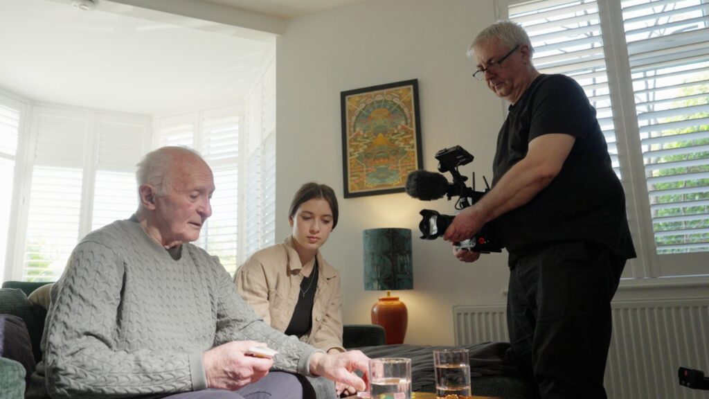 Cameraman filming an elderly man and young woman seated together in a home living room