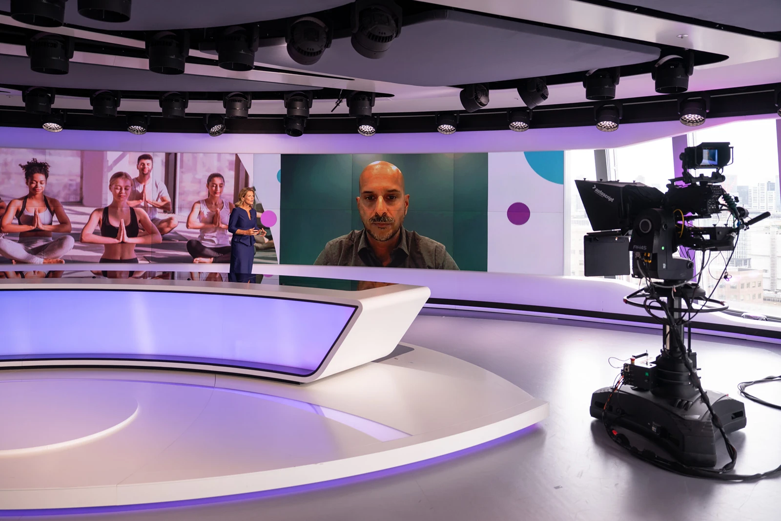 TV news anchor conducting remote interview beside yoga backdrop and studio camera equipment